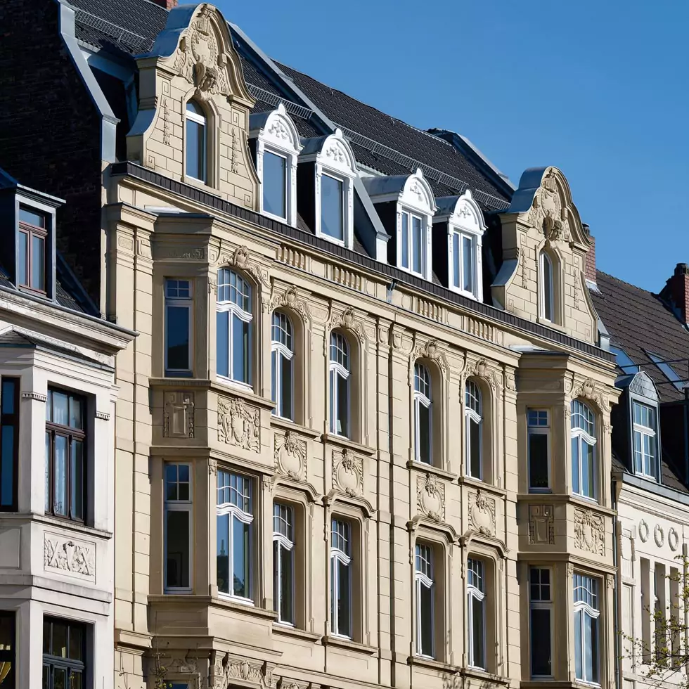 Fassaden mehrerer Altbaugebäude mit verzierten Fensterrahmen und mehreren Stockwerken unter blauem Himmel.