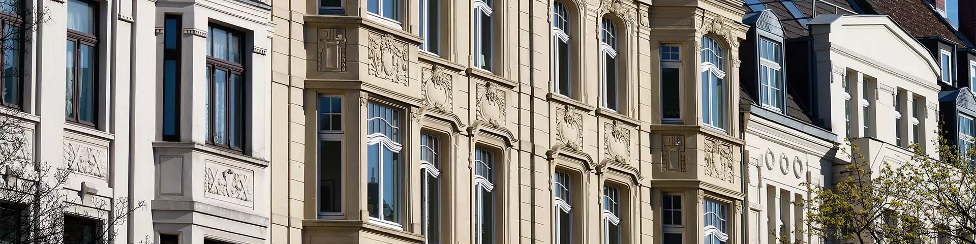 Fassaden mehrerer Altbaugebäude mit verzierten Fensterrahmen und mehreren Stockwerken unter blauem Himmel.