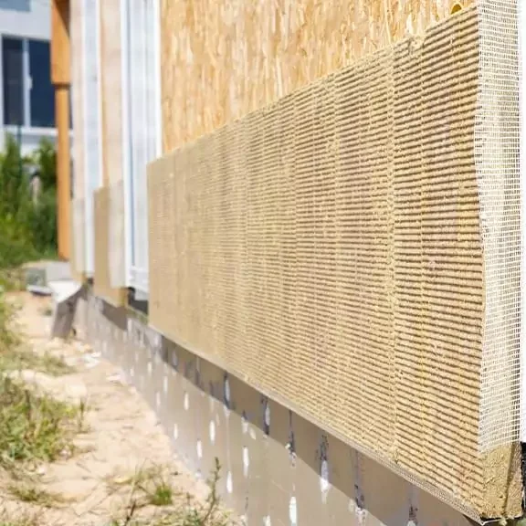 Fassade eines Hauses mit aufgebrachter Dämmung aus Holzfasermatten neben einem weißen Fensterrahmen.